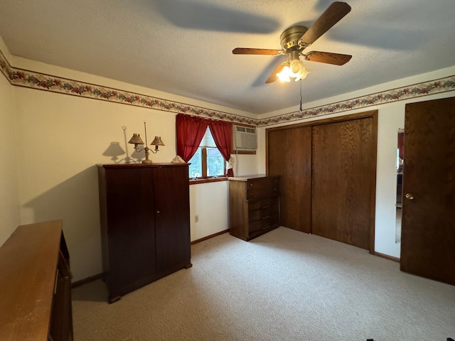 unfurnished bedroom featuring light carpet, a textured ceiling, a wall unit AC, ceiling fan, and a closet