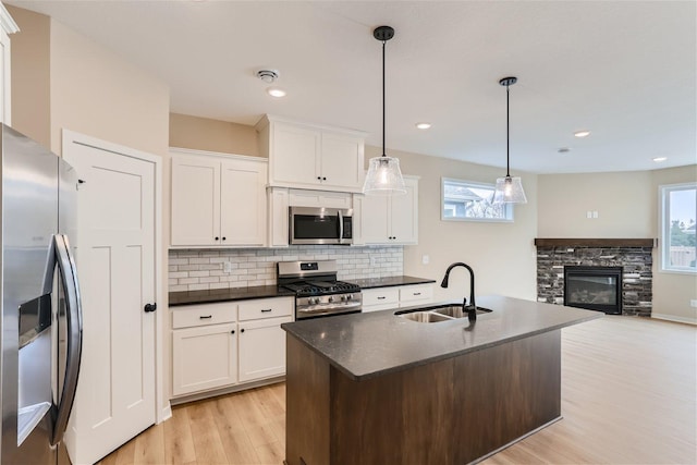 kitchen with appliances with stainless steel finishes, light wood-type flooring, sink, white cabinets, and hanging light fixtures