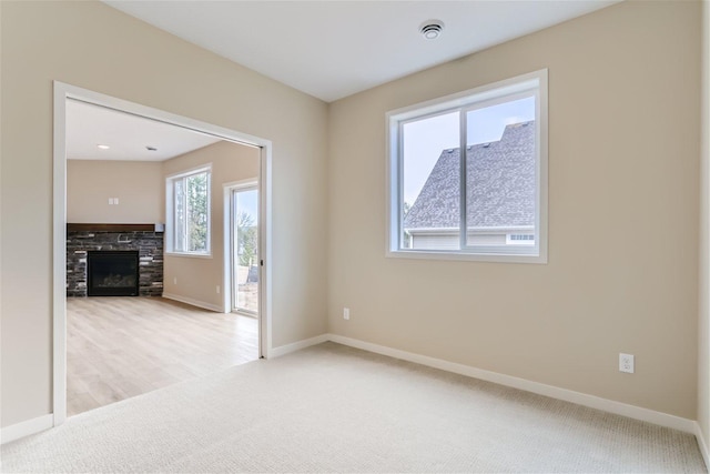 unfurnished room with a stone fireplace and light colored carpet