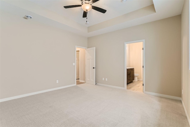 unfurnished bedroom featuring light carpet, a tray ceiling, ensuite bath, and ceiling fan