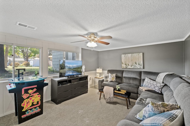 living room featuring light carpet, a textured ceiling, ceiling fan, and ornamental molding