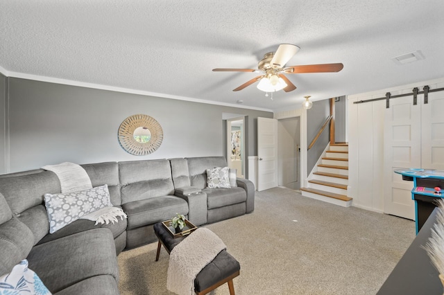 living room featuring ceiling fan, a barn door, crown molding, a textured ceiling, and light carpet