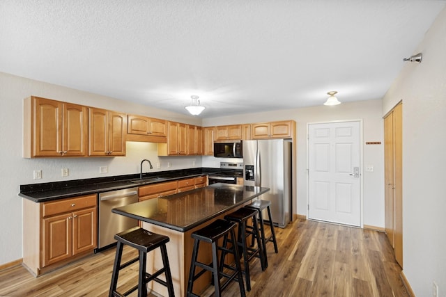 kitchen with sink, appliances with stainless steel finishes, a kitchen bar, a kitchen island, and light wood-type flooring