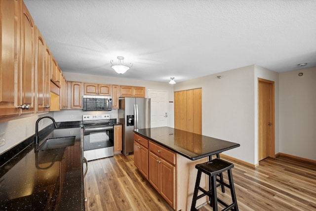 kitchen featuring a kitchen breakfast bar, stainless steel appliances, sink, wood-type flooring, and a kitchen island