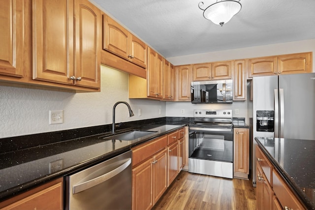 kitchen featuring sink, dark stone counters, a textured ceiling, appliances with stainless steel finishes, and hardwood / wood-style flooring