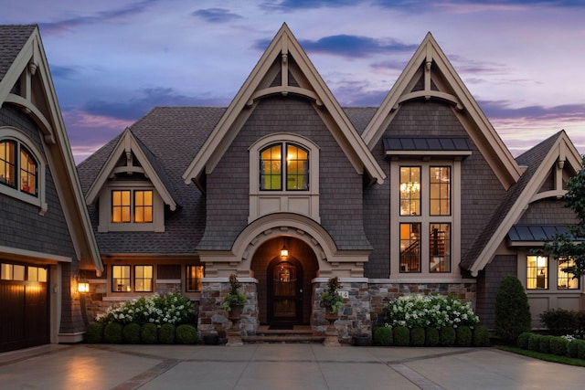 shingle-style home featuring a standing seam roof, stone siding, driveway, and a shingled roof