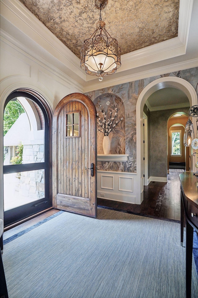 foyer entrance featuring arched walkways, crown molding, a tray ceiling, and wood-type flooring