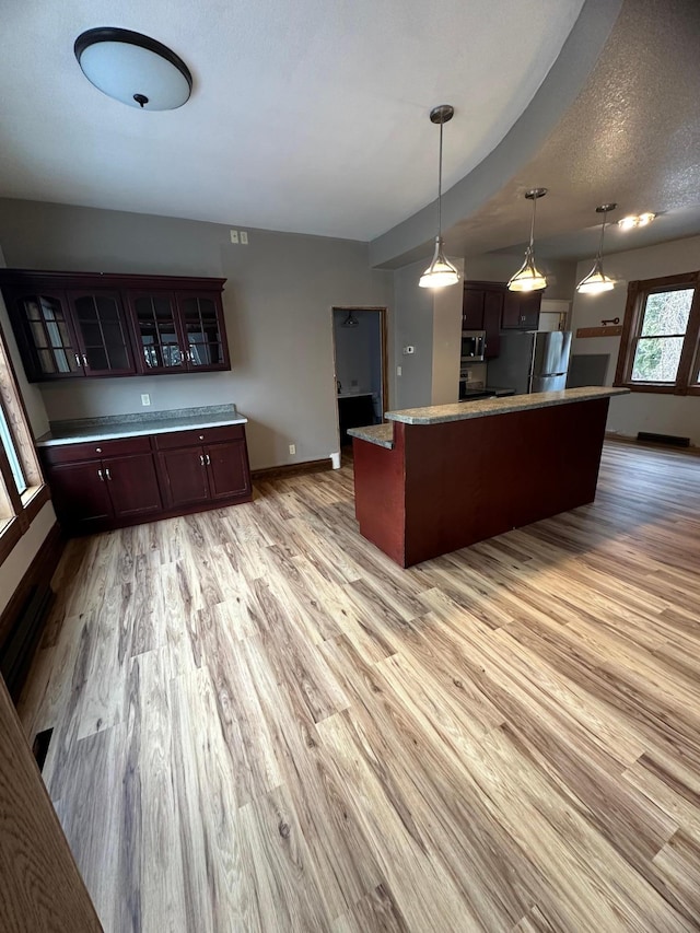 kitchen with a textured ceiling, stainless steel appliances, decorative light fixtures, light hardwood / wood-style floors, and a kitchen island