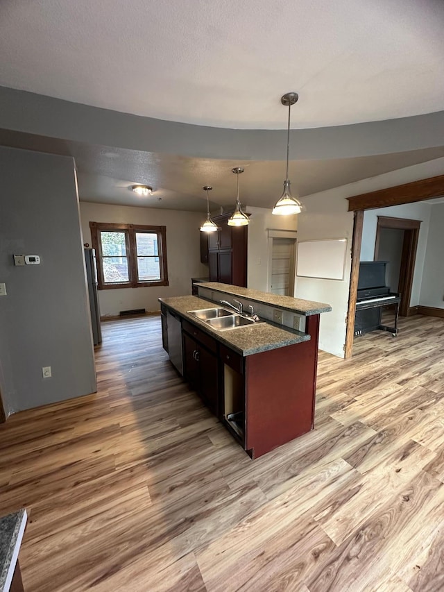 kitchen featuring dishwasher, sink, pendant lighting, light hardwood / wood-style floors, and a kitchen island with sink