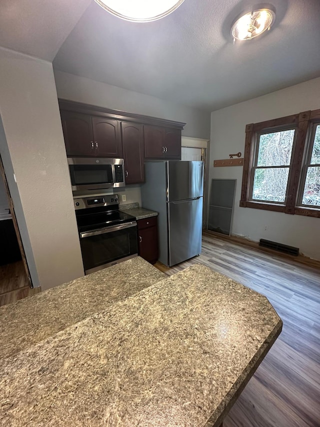 kitchen with light stone countertops, dark brown cabinets, light hardwood / wood-style flooring, and appliances with stainless steel finishes