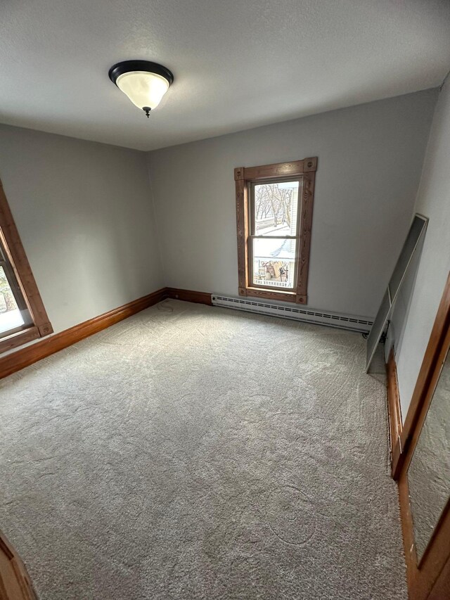 unfurnished room featuring carpet flooring, a healthy amount of sunlight, baseboard heating, and a textured ceiling