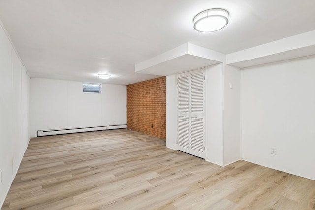 basement featuring light wood-type flooring, baseboard heating, and brick wall