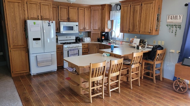 kitchen with kitchen peninsula, white appliances, dark wood-type flooring, and a breakfast bar area