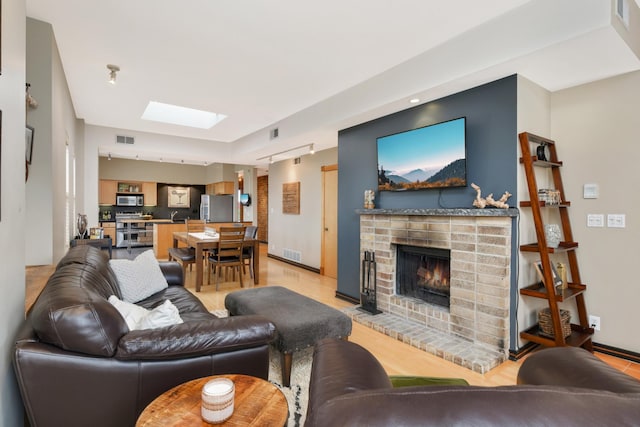 living room featuring a fireplace, a skylight, and light hardwood / wood-style flooring