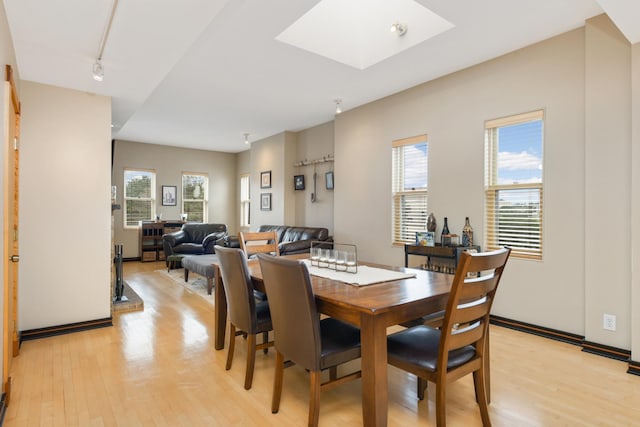 dining area featuring track lighting, a healthy amount of sunlight, light wood-type flooring, and a skylight