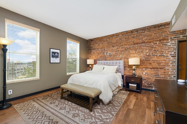 bedroom with hardwood / wood-style floors, multiple windows, and brick wall