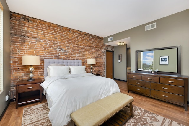 bedroom with light wood-type flooring and brick wall