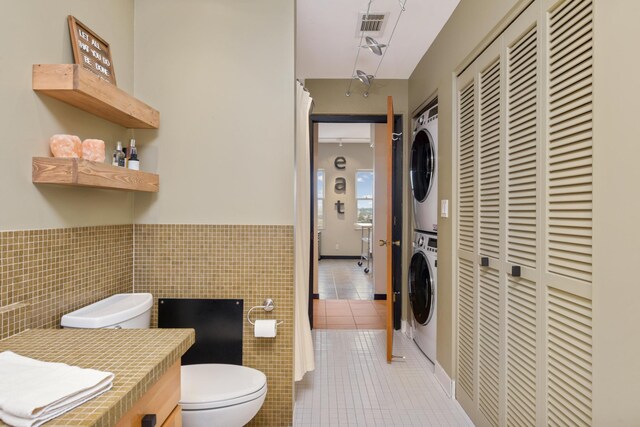 bathroom with tile patterned floors, vanity, tile walls, stacked washer and clothes dryer, and toilet