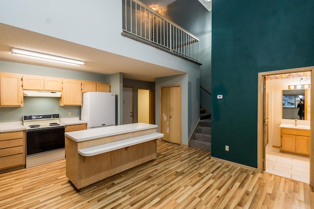 kitchen with light brown cabinets, white appliances, sink, light hardwood / wood-style flooring, and a towering ceiling