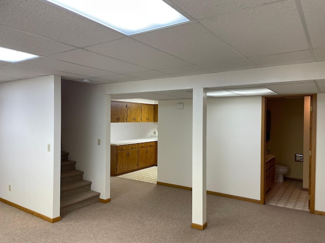 basement with a paneled ceiling and light colored carpet