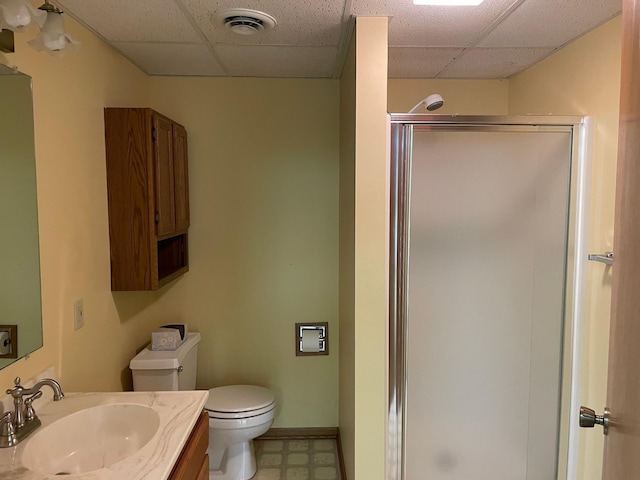 bathroom with a drop ceiling, toilet, an enclosed shower, and vanity