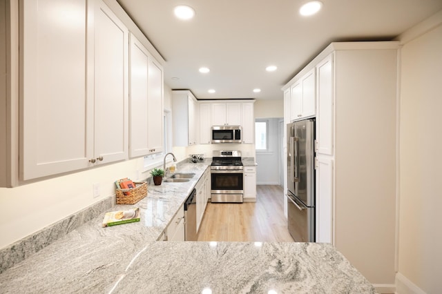 kitchen featuring white cabinets, sink, light wood-type flooring, light stone counters, and stainless steel appliances