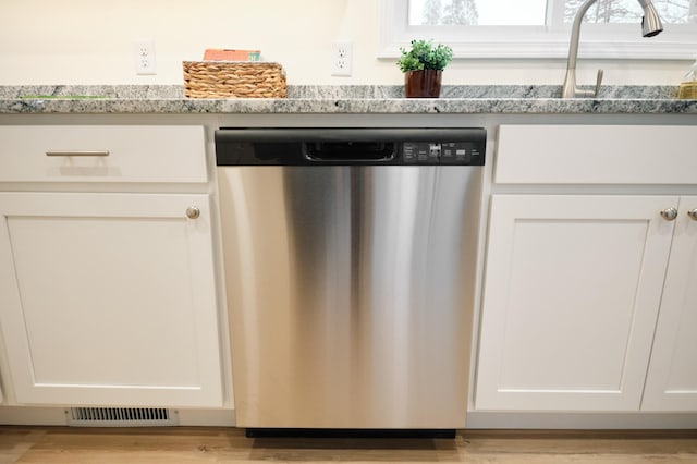 kitchen with light stone countertops, dishwasher, white cabinets, and light hardwood / wood-style floors