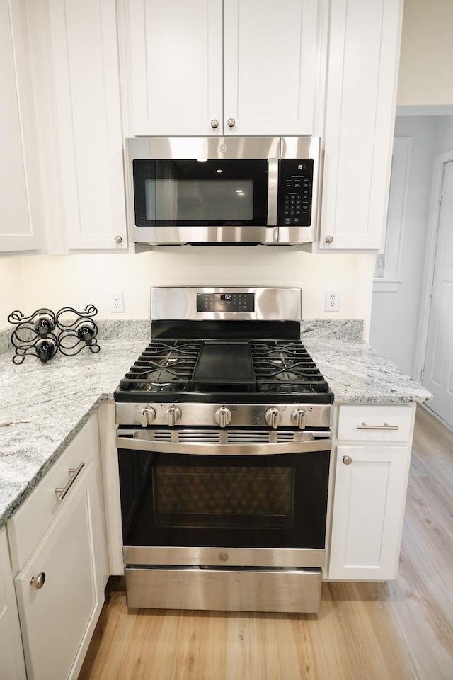 kitchen featuring light stone countertops, white cabinetry, stainless steel appliances, and light hardwood / wood-style floors