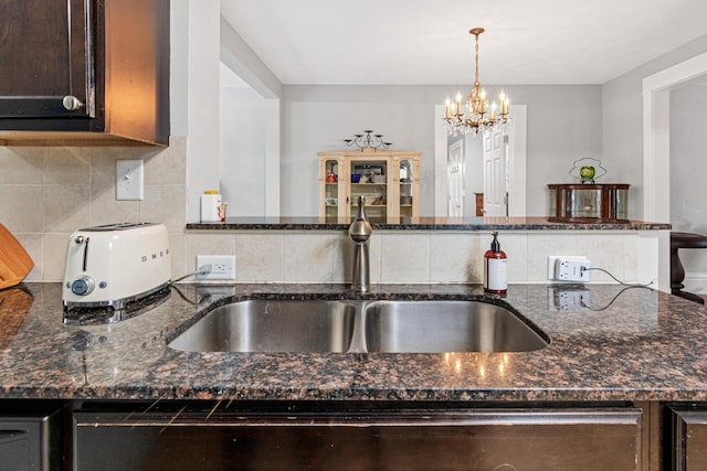 kitchen featuring sink, tasteful backsplash, a chandelier, pendant lighting, and dark stone counters