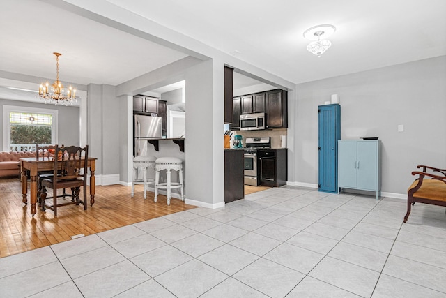 kitchen featuring dark brown cabinetry, light tile patterned floors, a chandelier, and appliances with stainless steel finishes