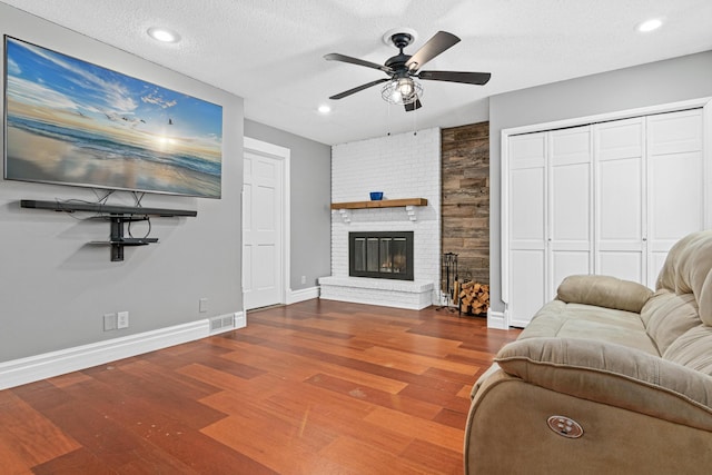 living room with a brick fireplace, wood-type flooring, a textured ceiling, and ceiling fan