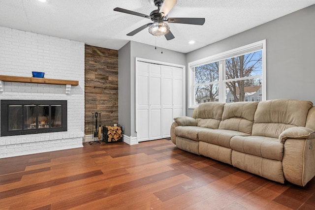 living room with dark hardwood / wood-style flooring, ceiling fan, a fireplace, and a textured ceiling