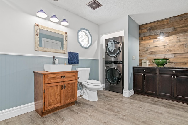 bathroom featuring hardwood / wood-style floors, stacked washer / dryer, vanity, a textured ceiling, and wood walls