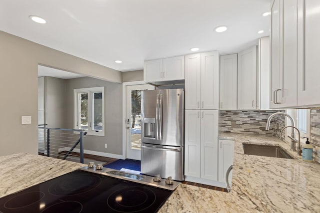 kitchen featuring light stone counters, white cabinets, a sink, and stainless steel refrigerator with ice dispenser