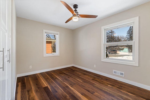 unfurnished room featuring a healthy amount of sunlight, baseboards, visible vents, and dark wood-style flooring