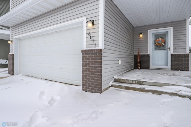 snow covered property entrance featuring a garage