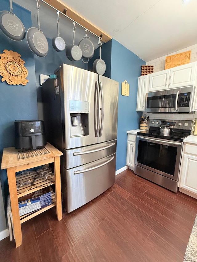 kitchen with appliances with stainless steel finishes, backsplash, white cabinetry, and dark hardwood / wood-style flooring