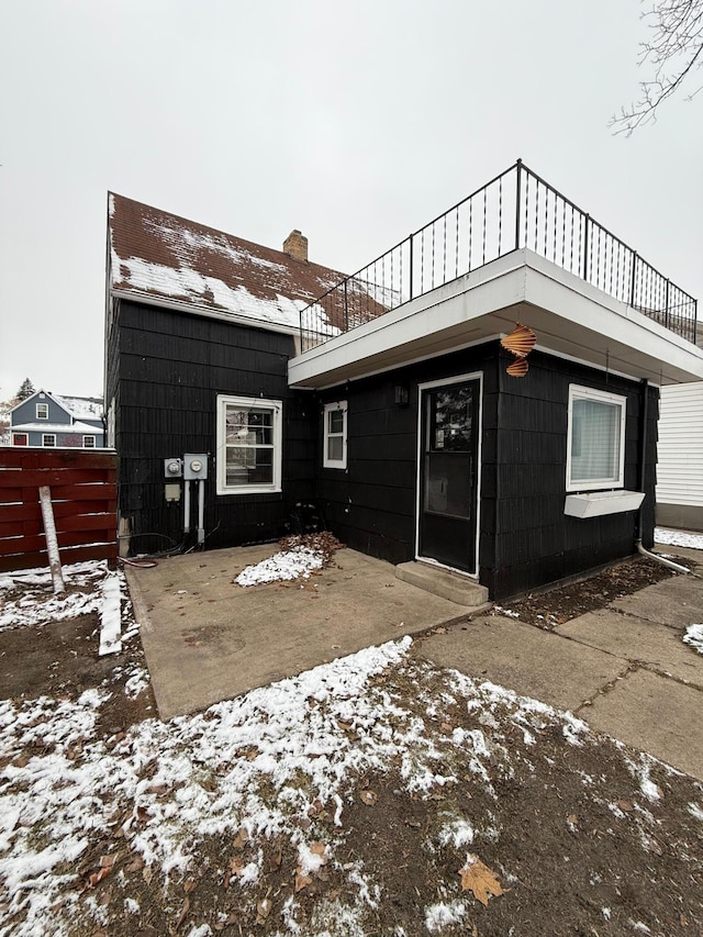 snow covered rear of property featuring a patio and a balcony