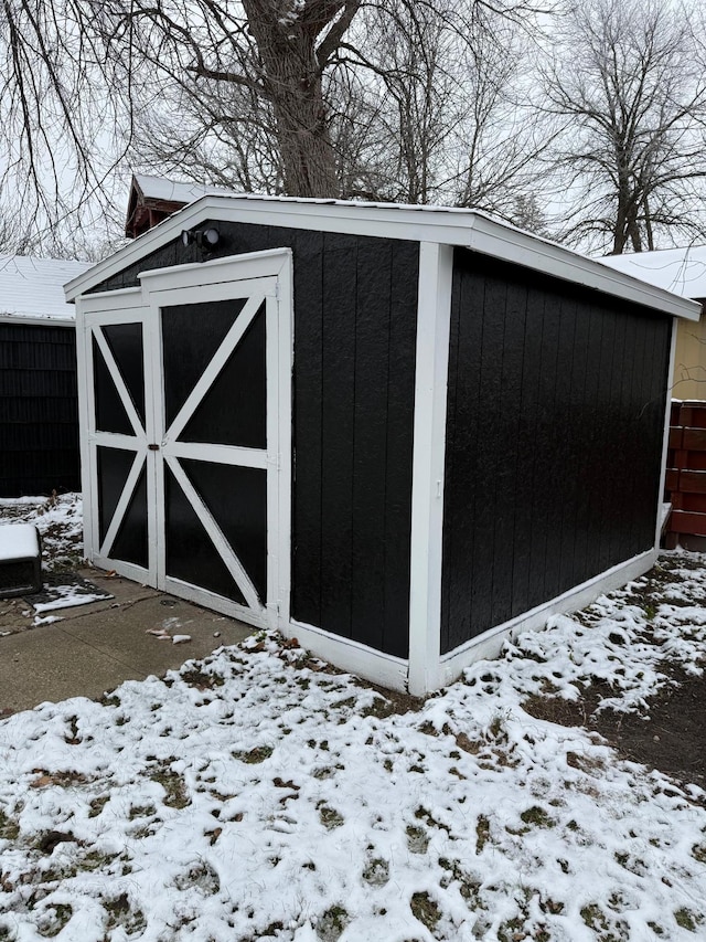 snow covered structure with an outdoor structure, fence, and a storage unit