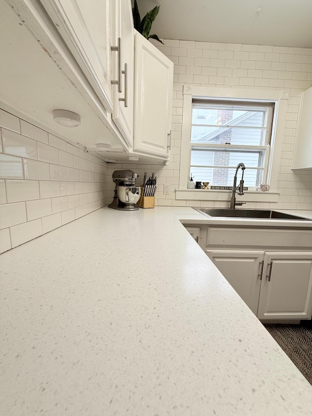 kitchen with a sink, backsplash, white cabinets, and light countertops