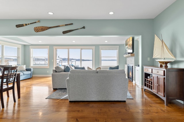 living room with a glass covered fireplace, recessed lighting, baseboards, and wood finished floors