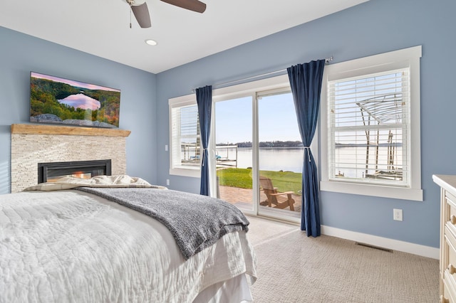 bedroom with baseboards, a water view, light carpet, a fireplace, and access to outside