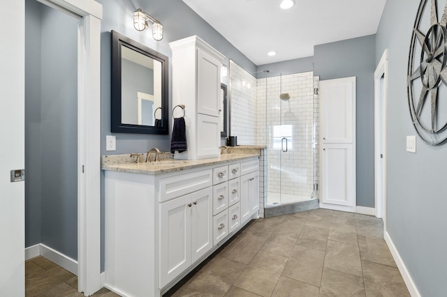 bathroom featuring tile patterned flooring, a shower stall, baseboards, double vanity, and a sink