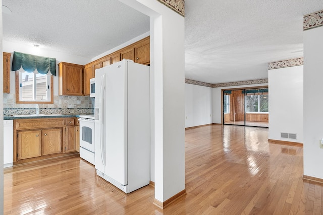 kitchen featuring white appliances, a textured ceiling, a wealth of natural light, and light hardwood / wood-style flooring