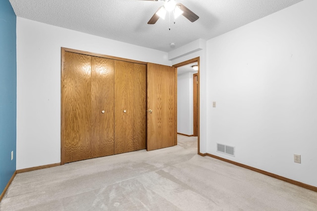 unfurnished bedroom featuring ceiling fan, a textured ceiling, light carpet, and a closet