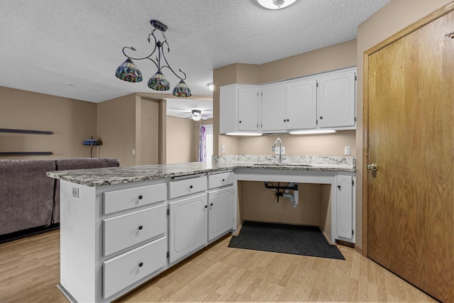 kitchen with kitchen peninsula, sink, light hardwood / wood-style flooring, white cabinetry, and hanging light fixtures