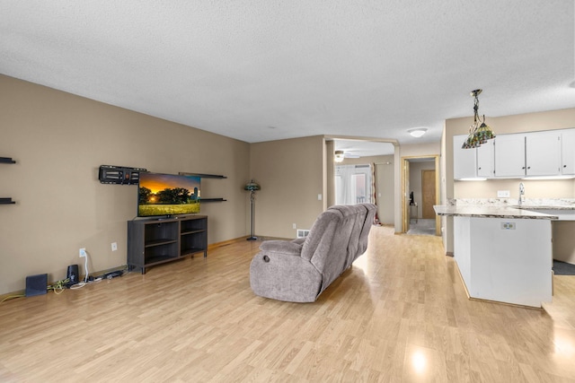 living room with ceiling fan, light wood-type flooring, and a textured ceiling