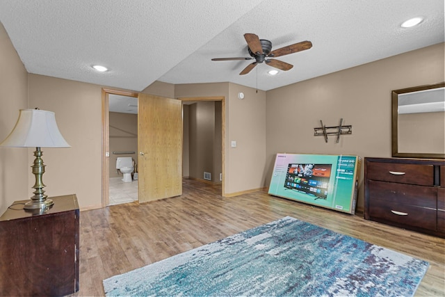 bedroom with a textured ceiling, light hardwood / wood-style floors, ceiling fan, and connected bathroom