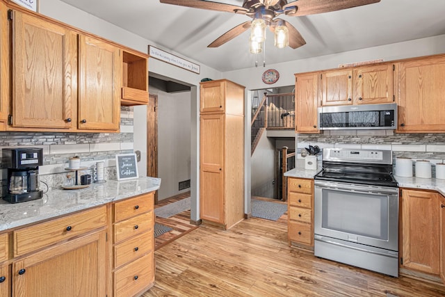 kitchen with backsplash, ceiling fan, light wood-type flooring, appliances with stainless steel finishes, and light stone counters