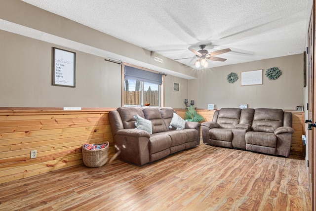 living room with a textured ceiling, light hardwood / wood-style floors, ceiling fan, and wooden walls